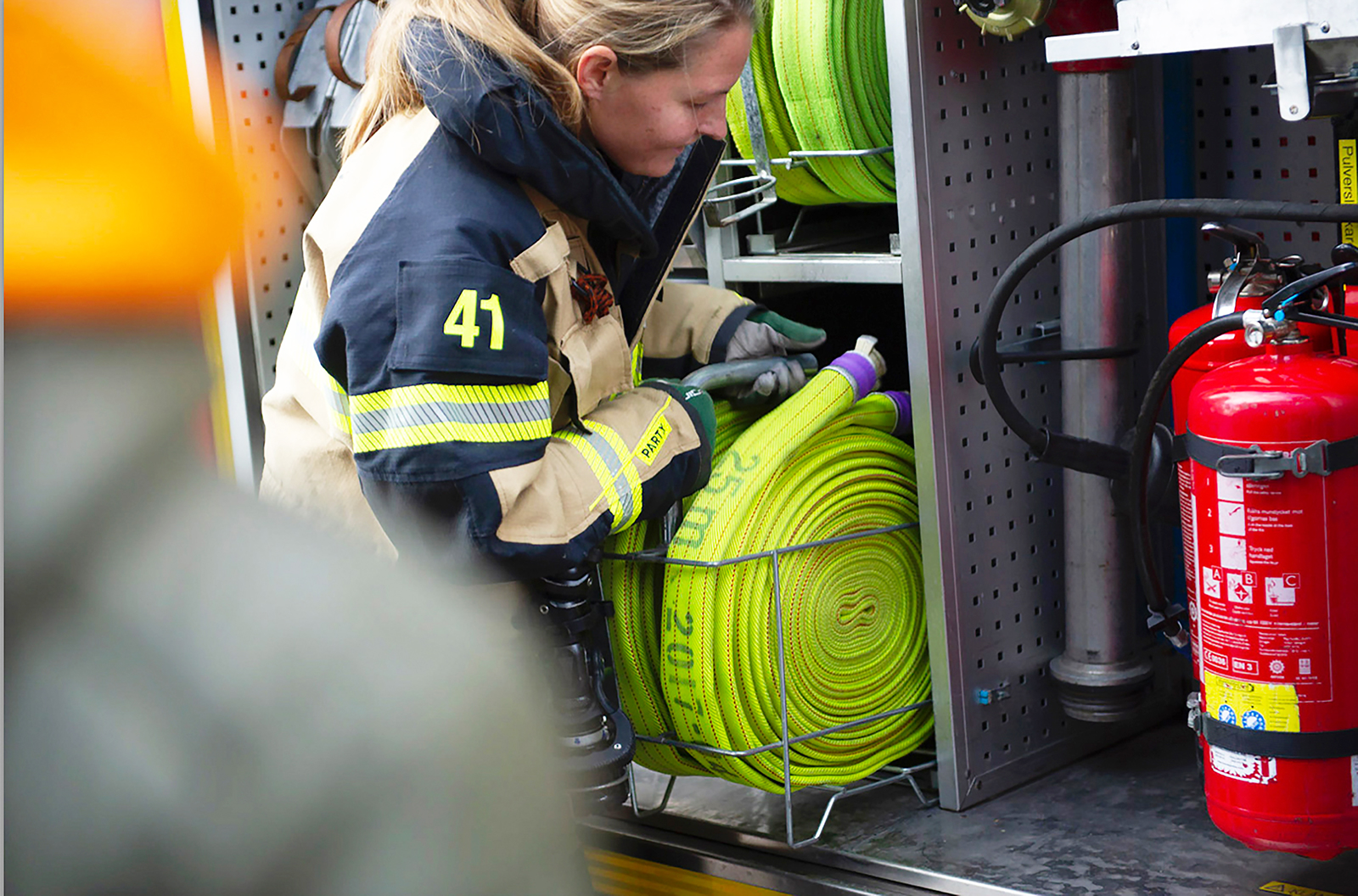 Brandman, kvinna lägger in hoprullad brandslang i brandbil.