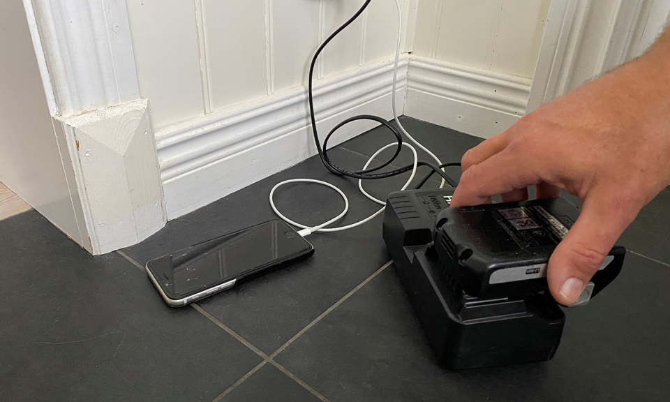 En mobiltelefon som ligger på ett stengolv och laddar samt ett litiumjonbatteri som läggs i en laddare.